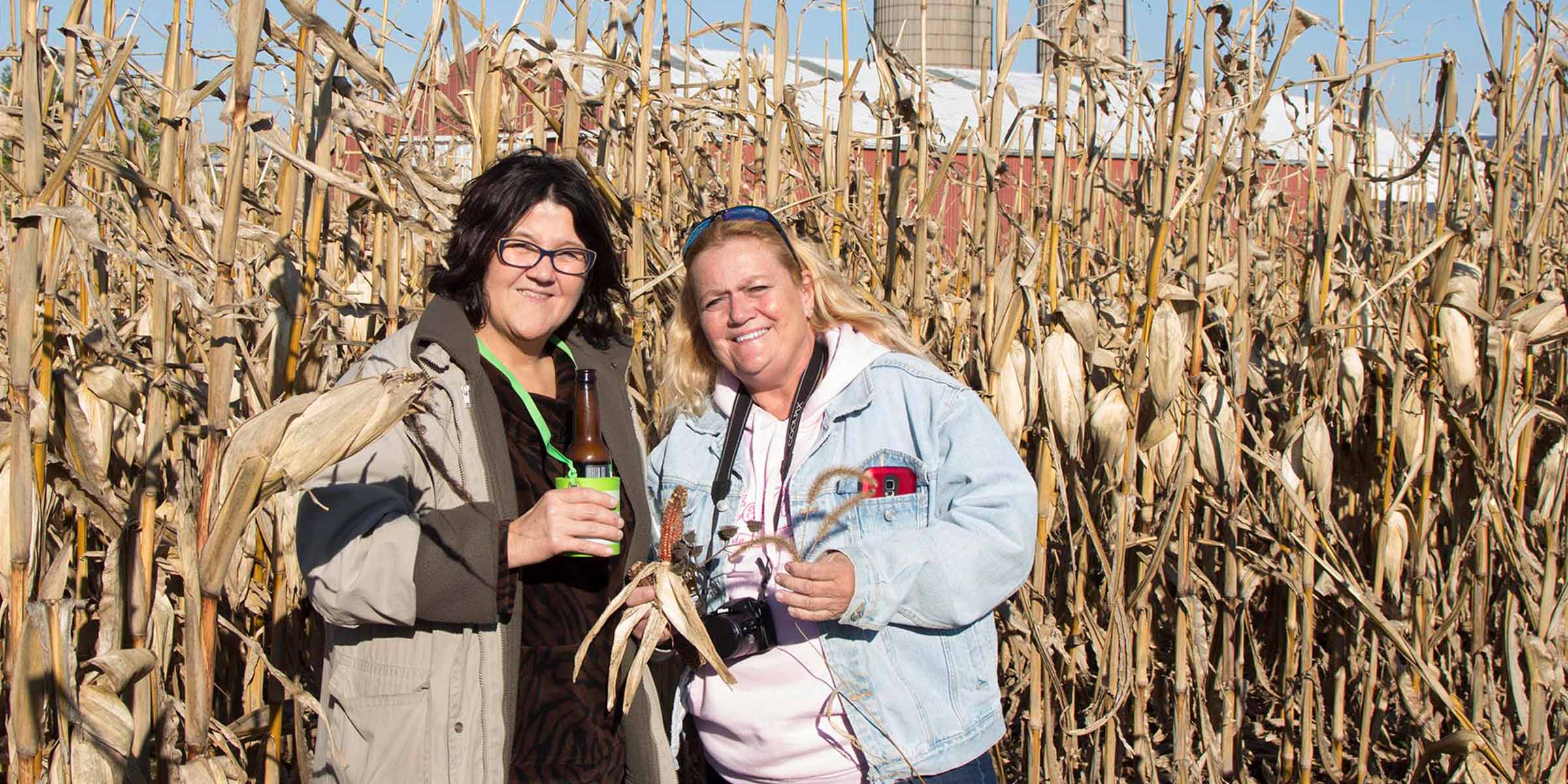 two women with drinks in a cornfield